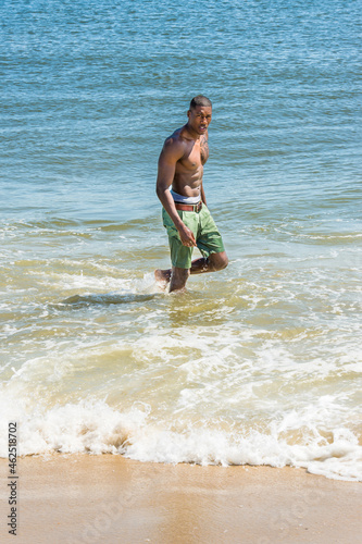 Obraz na płótnie A well built young sexy black guy, half naked, is walking on water of ocean, turning around, looking at you.. w salonie
