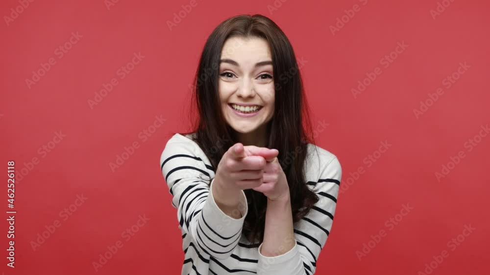 Woman pointing fingers on you looking at camera with toothy smile, congratulating with victory, wearing casual style long sleeve shirt. Indoor studio shot isolated on red background. Woman pointing fingers on you looking at camera with toothy smile, congratulating with victory, wearing casual style long sleeve shirt. Indoor studio shot isolated on red background.