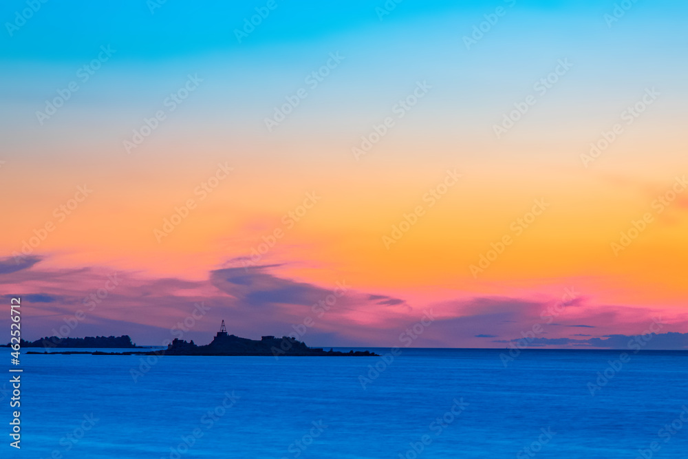 Silhouettes of buildings on the island against the colorful sea horizon.
