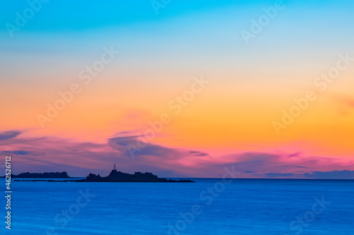 Silhouettes of buildings on the island against the colorful sea horizon. © FlyVi