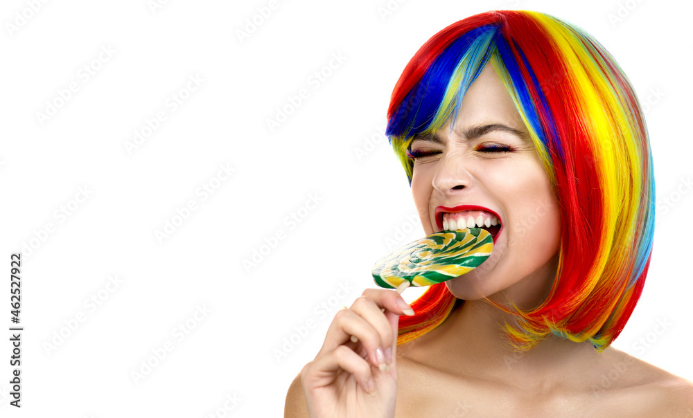 Lovely young woman with colored rainbow eyelashes, multi-color wig and bright makeup posing with a lollipop. Beautiful fashion model with professional creative color makeup