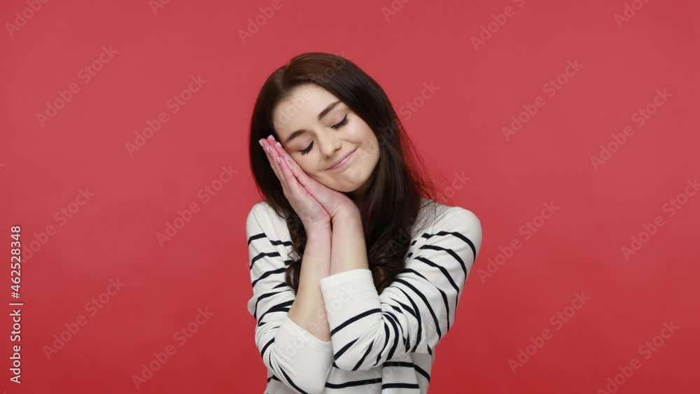Portrait of woman standing with closed eyes standing with arms under her head like pillow and sleep, wearing casual style long sleeve shirt. Indoor studio shot isolated on red background.