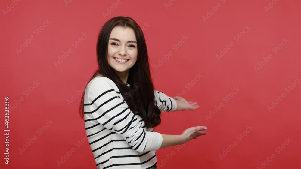Portrait of brunette happy woman opening her hands wide to embrace, welcoming friend, sharing love, wearing casual style long sleeve shirt. Indoor studio shot isolated on red background. Portrait of brunette happy woman opening her hands wide to embrace, welcoming friend, sharing love, wearing casual style long sleeve shirt. Indoor studio shot isolated on red background.