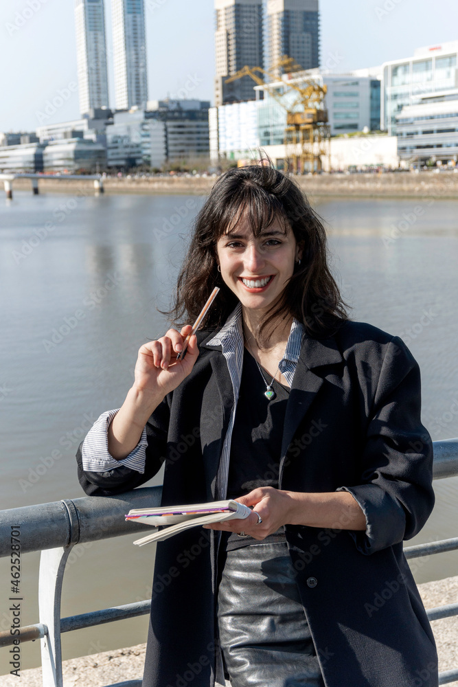 Fototapeta premium portrait of a young woman taking notes in the street and smiling