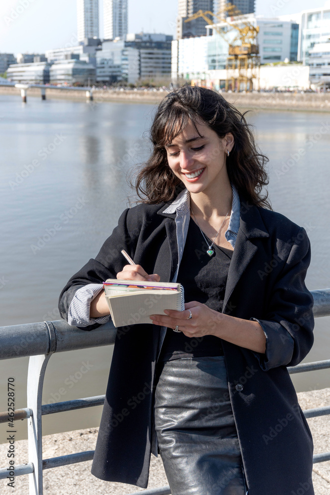 Fototapeta premium A young woman takes notes in a ring-bound notebook on the street