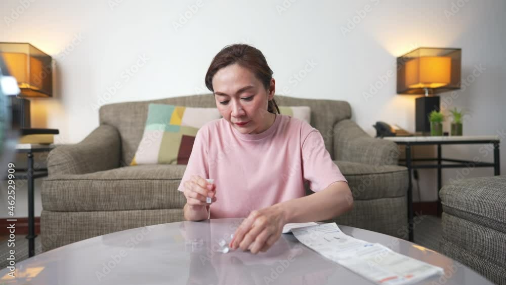4K Asian woman using rapid antigen test kit for self test COVID-19 epidemic at home. Adult female unpacking a swab for inserts into her nose. COVID-19 coronavirus pandemic protection concept.