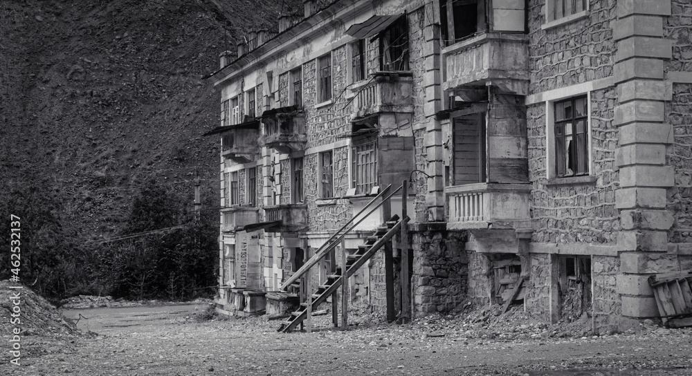 Black and white photo of old abandoned partially collapsed building with intricate stonework, ruined balconies, crashed windows. Desolation and destruction