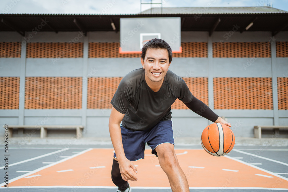 Naklejka premium a smiling male basketball player doing a low dribble between the legs dribble with the ball