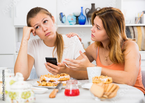 Portrait of female talking with sad girl friend with mobile at the kitchen
