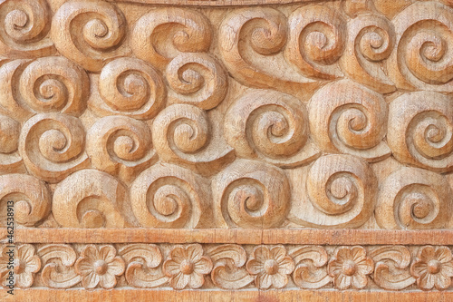 Pattern of flower and coiled spiral carved on teak wood background.