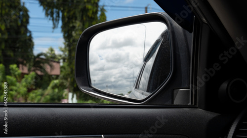Inside view of car can see mirror wing with glass. Look back in the mirror and see the side of the car, sky and clouds.
