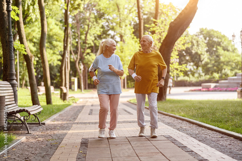 Happy mature woman with husband run along road in picturesque park