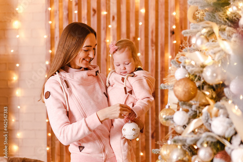 happy young mother holds a one-year-old baby girl near the Christmas tree. Christmas photo shoot
