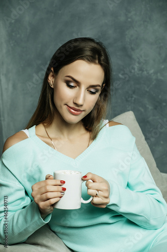 Beautiful and cute. Beautiful young woman holding coffee cup and sitting on chair at home. Lifestyle concept.