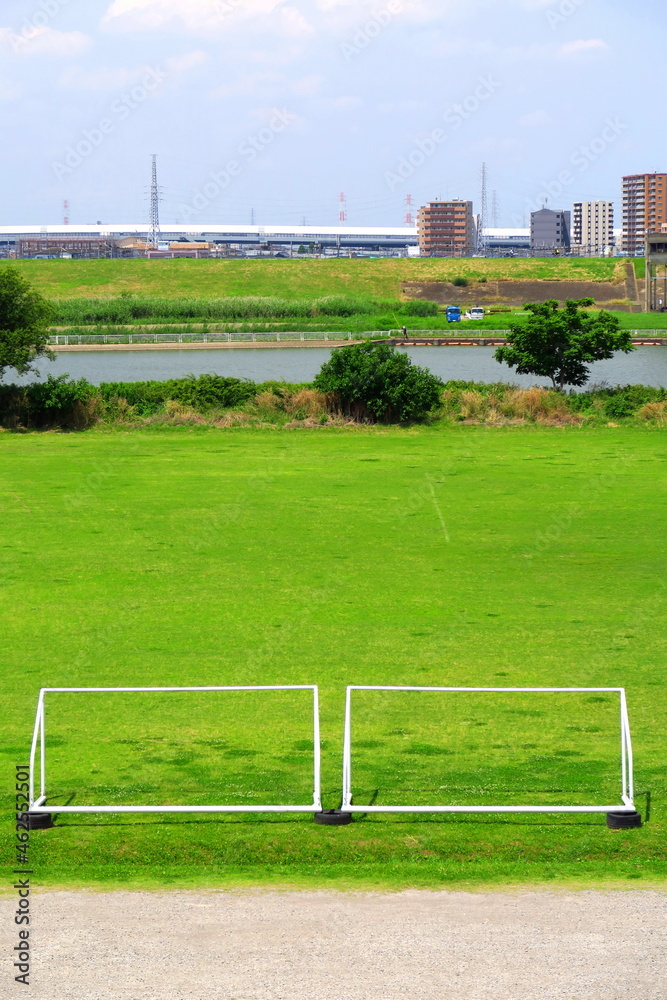 Obraz premium 土手から見る初夏のゴールポストのある江戸川河川敷のサッカー場と江戸川風景