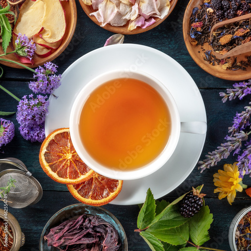 Tea, overhead square shot. Leaves, flowers and fruit around a cup of tea on a dark rustic wooden background