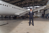 Handsome pilot in a black suit standing in angrar against the background of the airplane