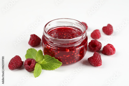 Jar of raspberry jam with ingredients on white background