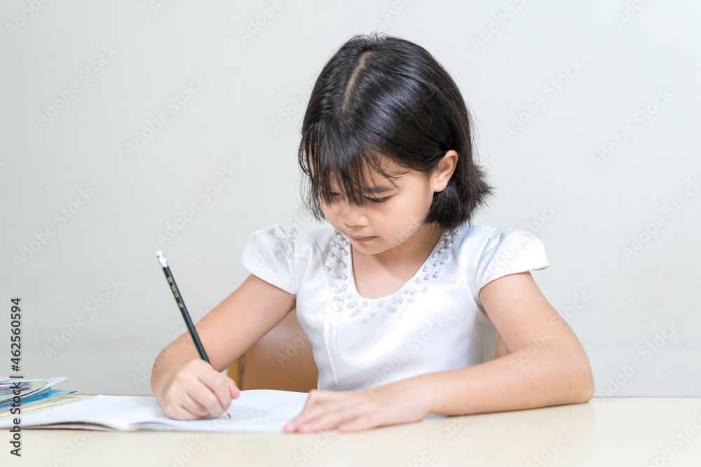 Cheerful Asian little girl children student writing on notebook doing homework and self study at home. Education Homeschool Concept Stock Photo Cheerful Asian little girl children student writing on notebook doing homework and self study at home. Education Homeschool Concept Stock Photo