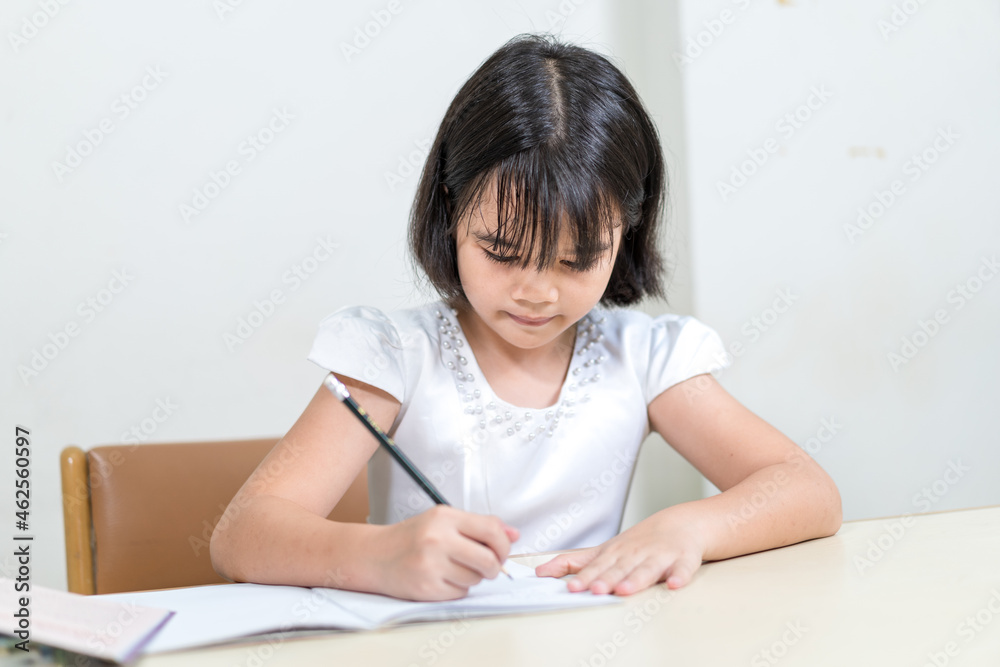 Cheerful Asian little girl children student writing on notebook doing homework and self study at home. Education Homeschool Concept Stock Photo Cheerful Asian little girl children student writing on notebook doing homework and self study at home. Education Homeschool Concept Stock Photo