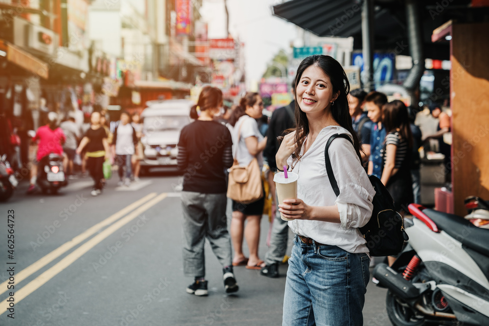 sunset time travel lifestyle concept. elegant asian japanese woman face camera smiling while holding cup of boba milk tea. lady tourist enjoy bubble drink on summer fair street on sunny day outdoors
