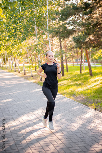 A girl in a black sports uniform is jogging in the evening park. Self-sports concept.
