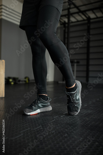 Sport background, close up of runner's legs and feet in black tracksuit and sport shoes, warming up indoor at gym against monkey bars background, practicing alone. People and active leisure time