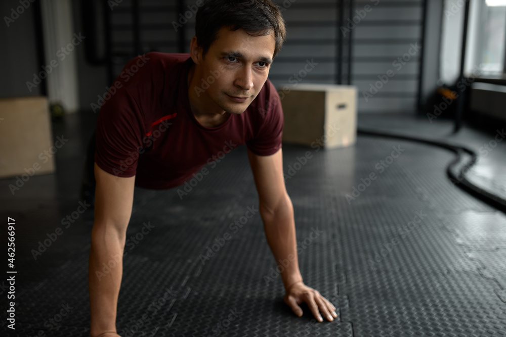 Sportive Caucasian man doing plank core exercise with straight hands at gym, training back press muscles looking ahead with concentrated face expression. Active lifestyle concept. Crossfit, fitness Sportive Caucasian man doing plank core exercise with straight hands at gym, training back press muscles looking ahead with concentrated face expression. Active lifestyle concept. Crossfit, fitness