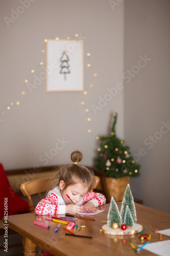 child writes letter to Santa Claus at home. little girl draws with crayons on background of Christmas devoration. photo