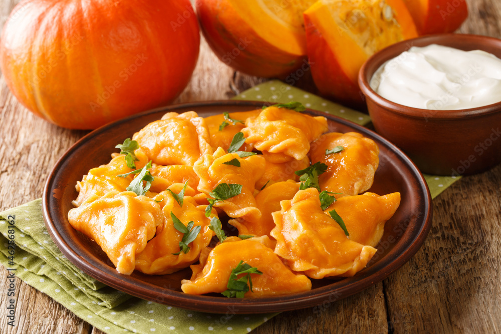 Delicious healthy orange pumpkin dumplings served with sour cream close-up in a plate on the table. horizontal