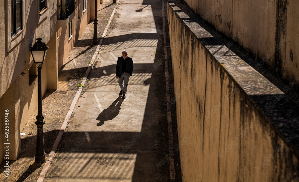 Man in black suit walking on path with sunlight and shadow Man in black suit walking on path with sunlight and shadow