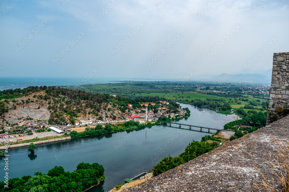 View from the wall of Rozafa Castle to the valley of the Buna River and the mountain-wooded panorama. Beautiful summer landscape with a village on the river bank against the background of stone walls