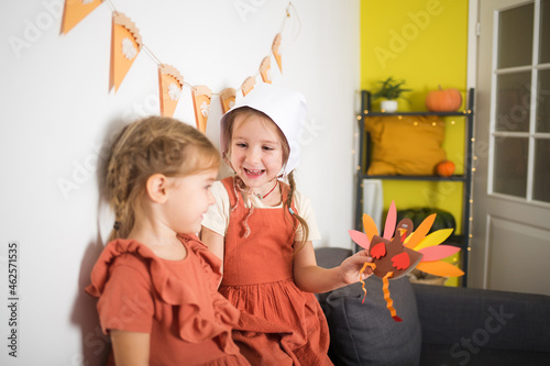 girl in suit shows toy on background of interior decor at home. paper craft for kids. DIY turkey made for thanksgiving day. create art for children.