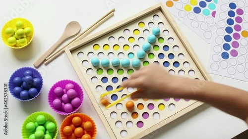 The child lays out colorful balls with tweezers. Wooden toy. Study of colors. Montessori concept, early brain exercise. Early education, fine motoric skills. Kids leisure. Preschool education. photo