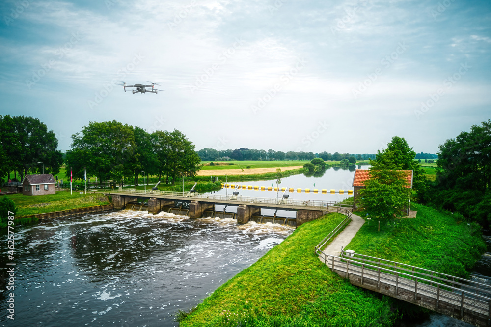 Water swirls from the weir in the river Vecht in the Netherlands. Downstream, Lock Keeper's House next to the bridge. Fish passage, Overijsselse Vecht, A flying drone in the blue sky Water swirls from the weir in the river Vecht in the Netherlands. Downstream, Lock Keeper's House next to the bridge. Fish passage, Overijsselse Vecht, A flying drone in the blue sky