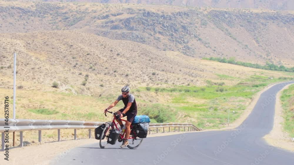 Static view caucasian male cycle solo on red bicycle uphill in extreme heat outdoors in scenic nature. Bicycle touring adventure lifestyle concept Static view caucasian male cycle solo on red bicycle uphill in extreme heat outdoors in scenic nature. Bicycle touring adventure lifestyle concept