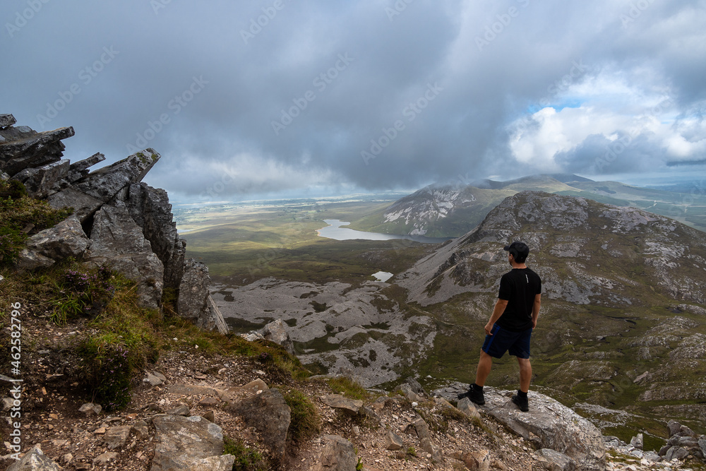 Man standing on top of mountain admiring landscape of Errigal mountain Co. Donegal Ireland