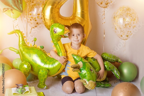 Little boy in room decorated for birthday party with baloons, large inflatable number 4, Dinosaur baloons.