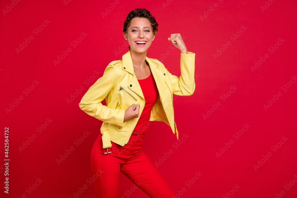 Photo of charming lucky young lady wear yellow jacket smiling rising fists isolated red color background Photo of charming lucky young lady wear yellow jacket smiling rising fists isolated red color background
