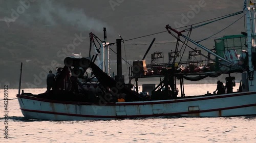Tracking shot of isherman silhouettes on fishing vessel during sunrise, 400mm