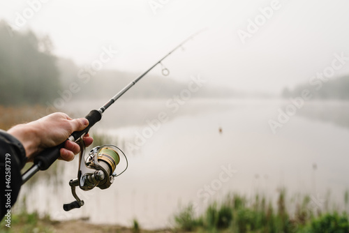 Fisherman with rod, spinning reel on river bank. Fishing for pike, perch, carp. Fog against the backdrop of lake. Background misty morning. wild nature. The concept of a rural getaway. Fishing day.