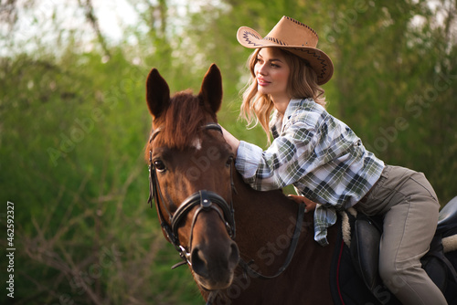 Beautiful girl in a hat riding a horse in countryside
