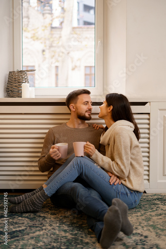 Romantic couple at home. An Attractive young woman and handsome man are enjoying spending time together while siting coddling with cups of tea in hands.