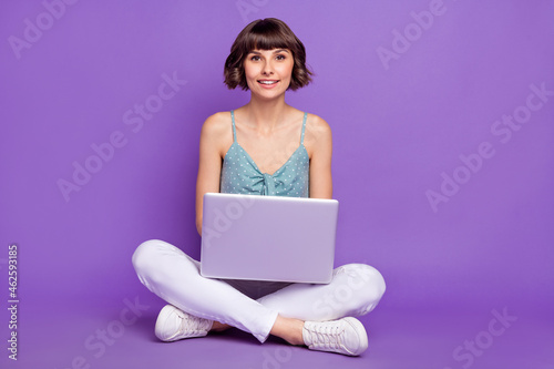 Portrait of attractive cheerful girl sitting using laptop typing email isolated over bright violet purple color background