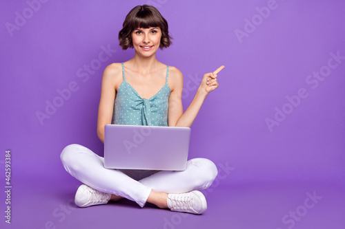 Portrait of lovely trendy cheerful girl sitting using laptop showing copy space isolated over bright violet purple color background