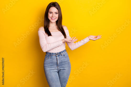 Photo of optimistic brunette lady stand point empty space wear pink shirt jeans isolated on yellow color background