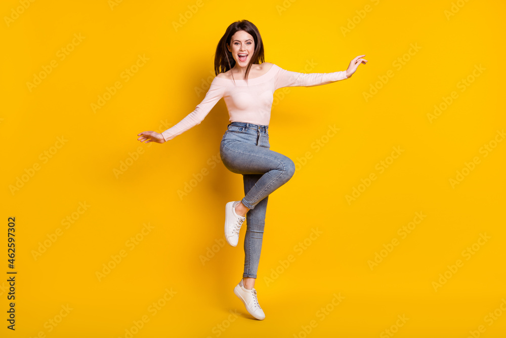 Full size photo of young fun excited smiling crazy girl jumping with flying hair isolated on yellow color background