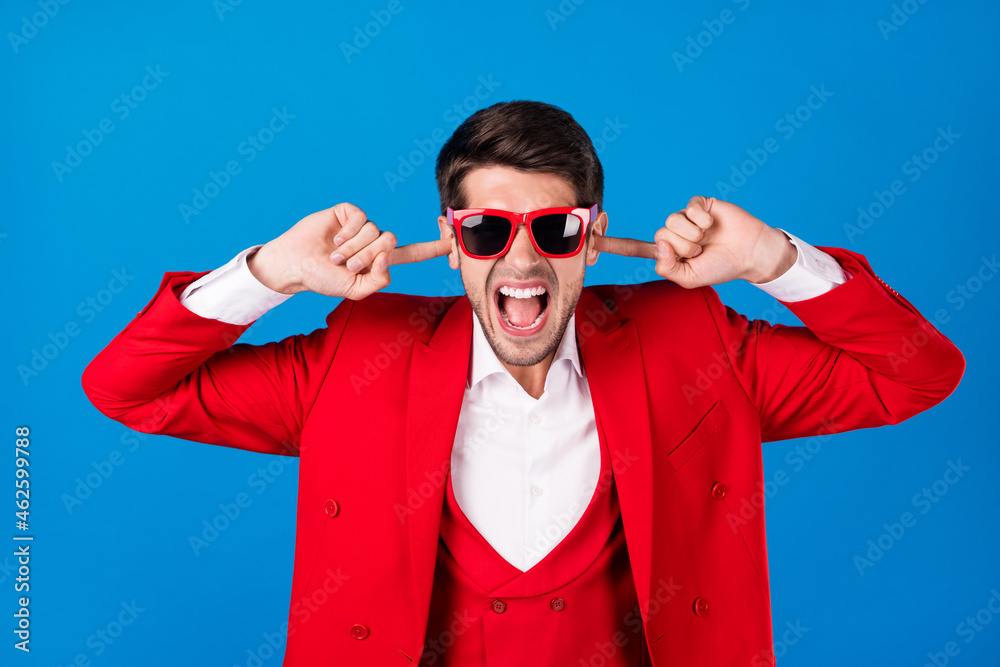 Photo of young man unhappy angry mad cover fingers ears loud noise mad isolated over blue color background Photo of young man unhappy angry mad cover fingers ears loud noise mad isolated over blue color background