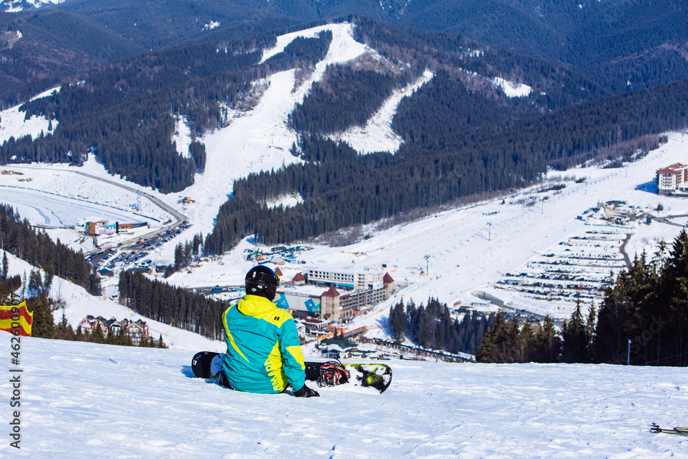 man sitting with snowboard on the top of the hill with beautiful view