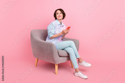 Full length body size photo woman sitting browsing internet on smartphone looking copyspace isolated pastel pink color background